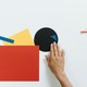 Contemporary artwork featuring geometric shapes in paper collage style with a hand interacting.
